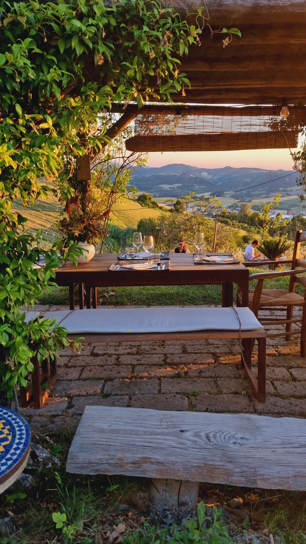 Tavolo apparecchiato sotto la pergola al tramonto, con vista sulle colline bolognesi